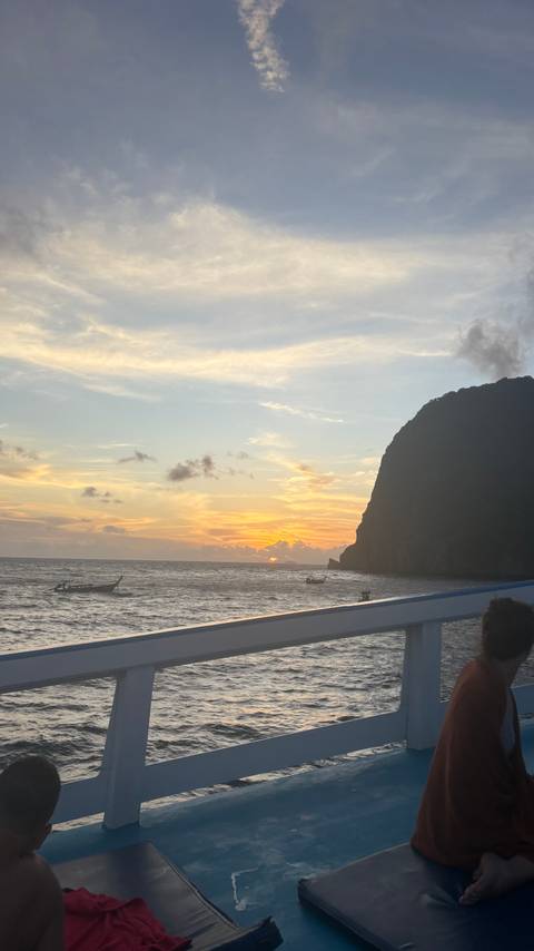 Sunset view over the sea with boats and a distant island cliff.