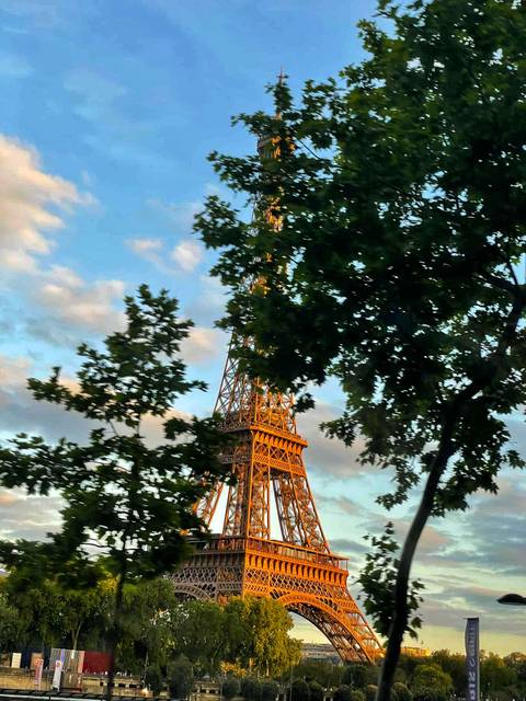 Eiffel Tower partially obscured by trees under a colorful sky.