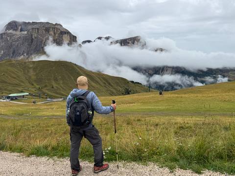 A person standing on a hillside with mountains shrouded in clouds.