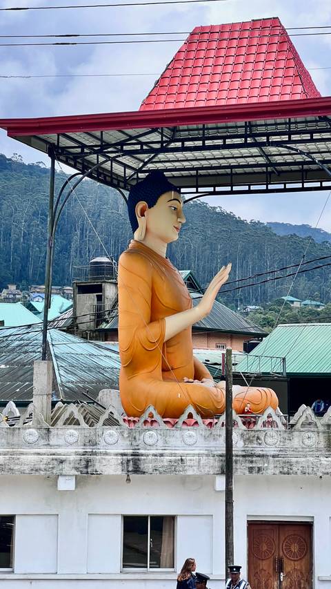 Large Buddha statue amidst rooftops and trees.