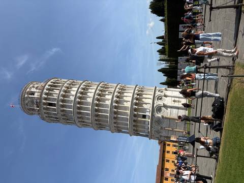 People taking photos at the leaning tower under a clear sky.