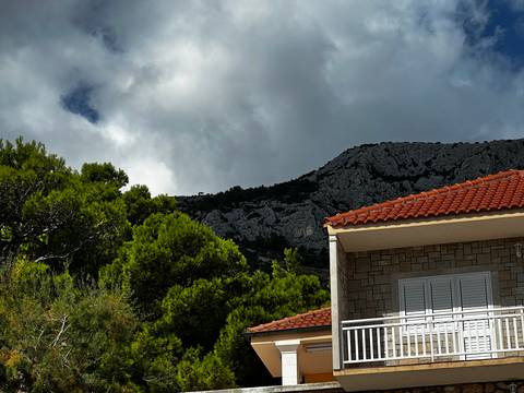 House with red roof tiles under a cloudy sky near mountains.