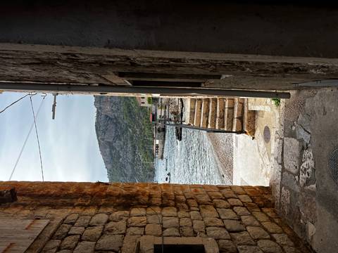 Narrow alleyway leading to a pebbled shore with boats.