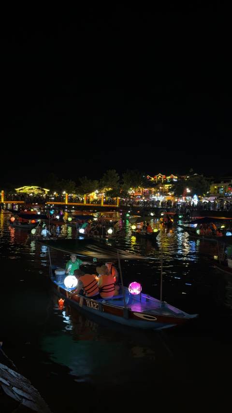       Colorful night scene of lantern-lit boats on a river.
  