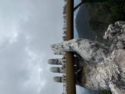       Golden Bridge with hand sculptures in foggy mountains.
  
