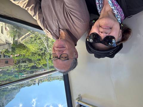       Two people smiling inside a transport with a view outside.
  