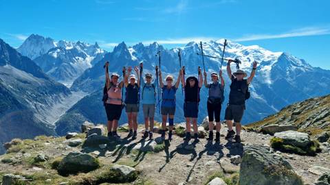 Group of hikers on a mountainous trail with snow-capped peaks in the background.