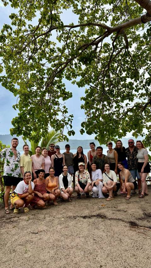 Group photo under trees with mountains in the background.
