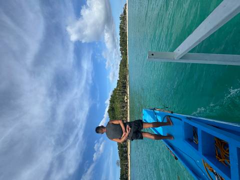 Person on a blue boat heading towards a tropical island.