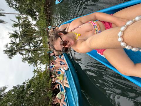 People riding on boats in a river with palms on the side.