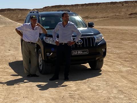 Two people standing by a car in a desert area.