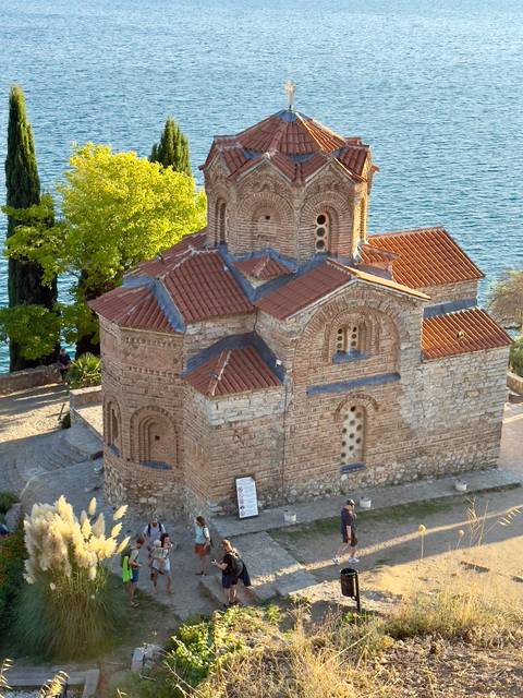 Small ancient church by the water with a red roof.