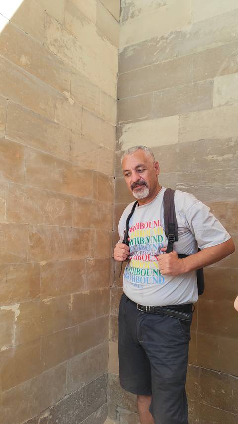 Man with a backpack standing against a stone wall.