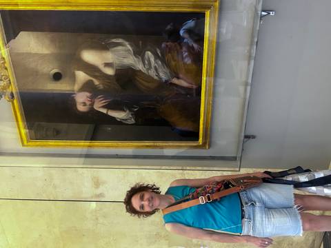       Person posing next to a classic painting in a museum.
  