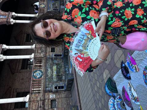       Person in Seville holding a decorated fan with scenic background.
  