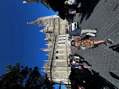       People posing in front of a historic building complex with a tall tower.
  