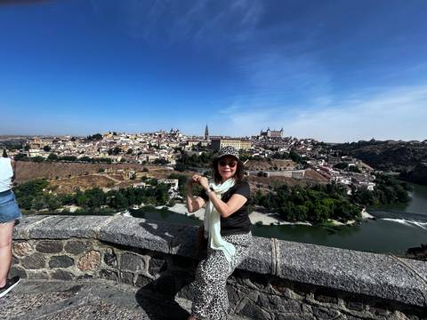       Woman posing by a stone wall with a view of a city across a river.
  