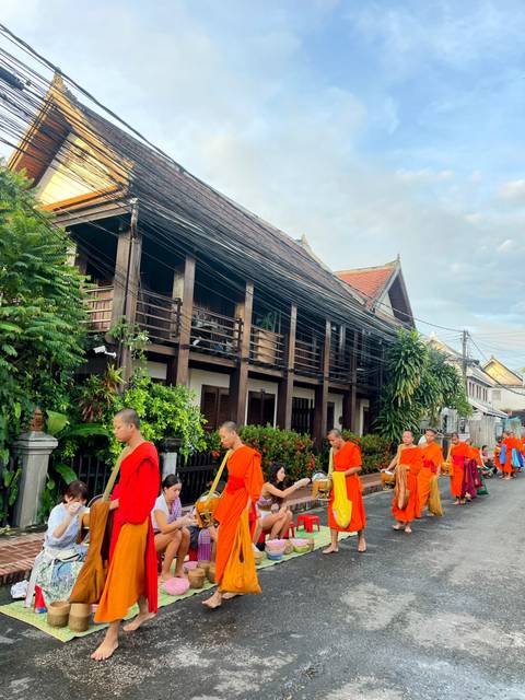       Monks in orange robes walking by a traditional wooden building.
  