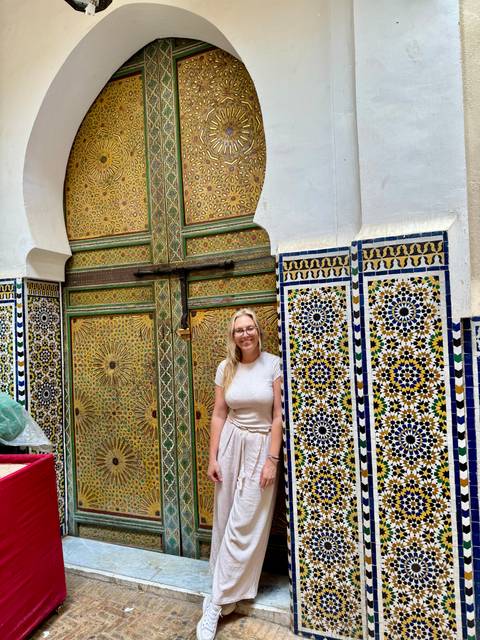 A tourist smiling in front of a beautifully decorated door with intricate tiles.