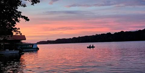 Sunset over a river with a small boat and silhouette of trees.