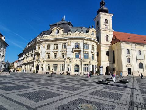       Plaza with large ornate buildings in sunny weather.
  