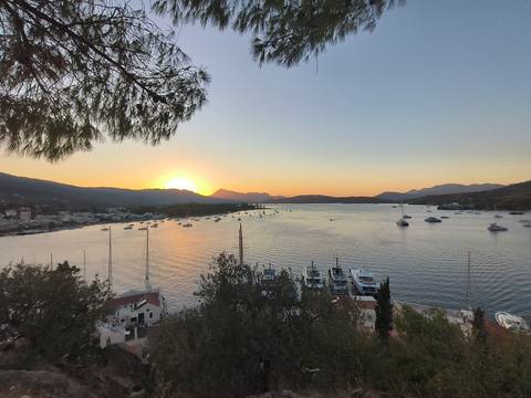 Sunset over a bay with sailboats and mountains.