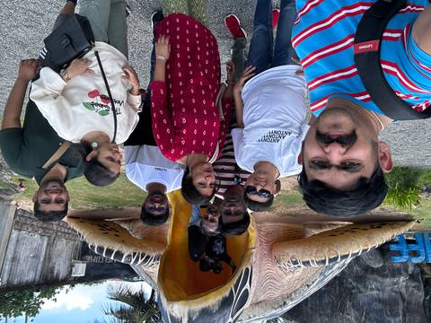 Tourists posing in front of a giant statue with a lush background.