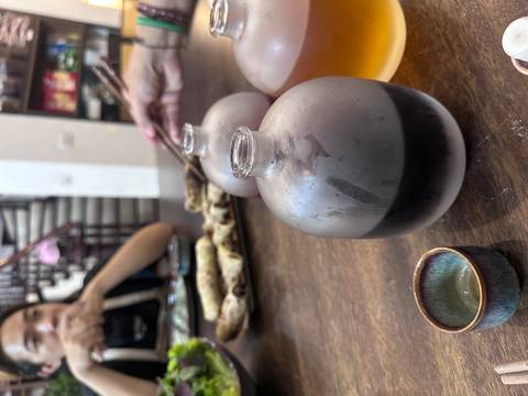 Glass bottles and small cups on a table with a person holding chopsticks.