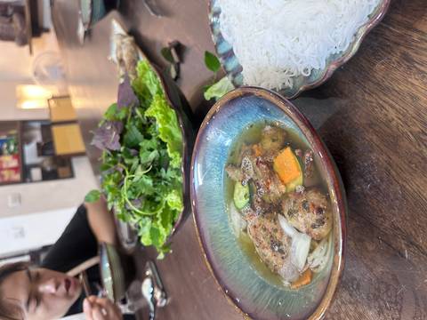 Vietnamese dish with a bowl of soup, greens, and noodles.