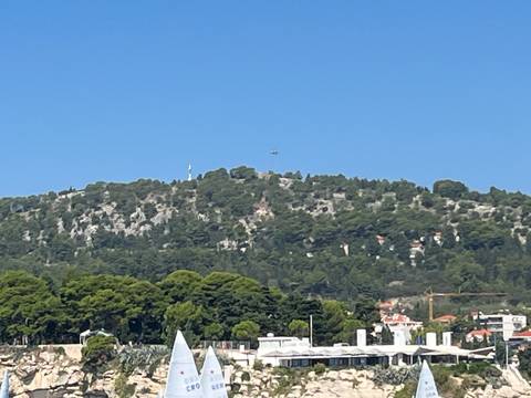 A forested hill viewed from a distance with a clear blue sky.