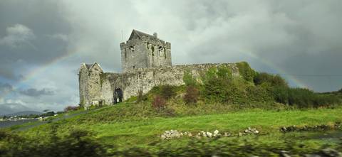 Stone castle with rainbow in cloudy sky.