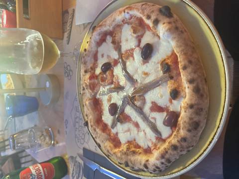 Pizza with anchovies and olives served with a drink.