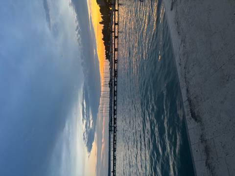 Sunset view over a pier with sailboats on the water.