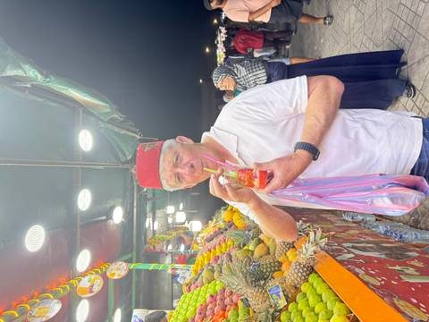       Man drinking juice at a vibrant market stall.
  