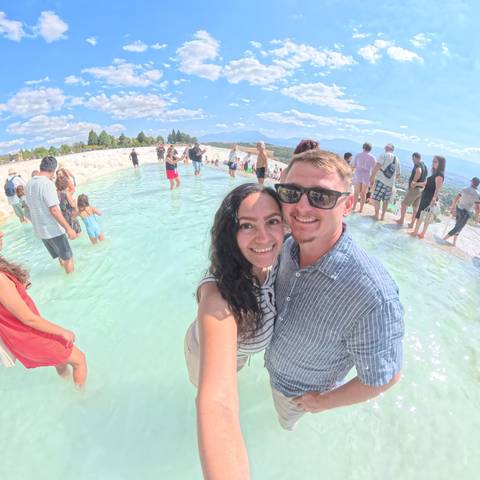       Couple smiling in natural hot springs with other tourists.
  
