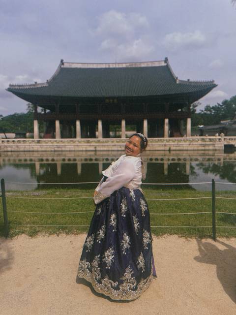Person in traditional hanbok posing by a pond.