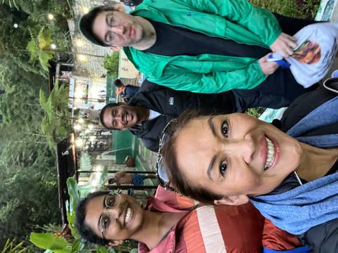Group of people smiling at a scenic outdoor location with trees and structures.