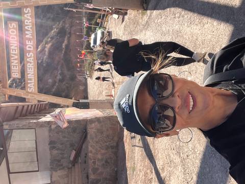 Woman taking a selfie at Salineras de Maras with people and signage in the background.