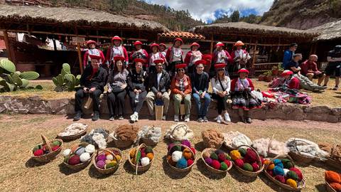 Group of people in traditional attire with displayed textiles and wool baskets at a historical site.