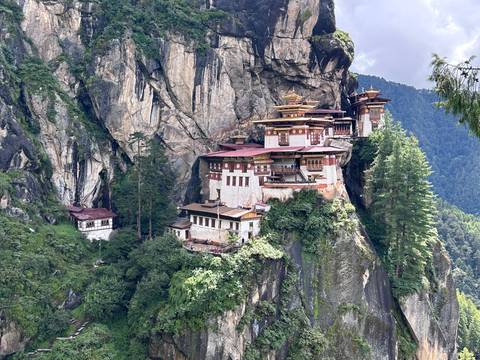 A monastery perched on a cliffside amidst lush green forests and mountains.