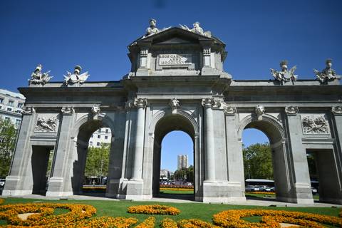 A historic stone arch with sculptures and engravings set against a bright blue sky.