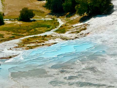 Thermal pools with turquoise water cascading down white travertine terraces.