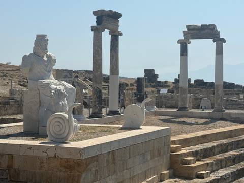 Ancient Greco-Roman ruins with columns, statues, and a seated deity statue.