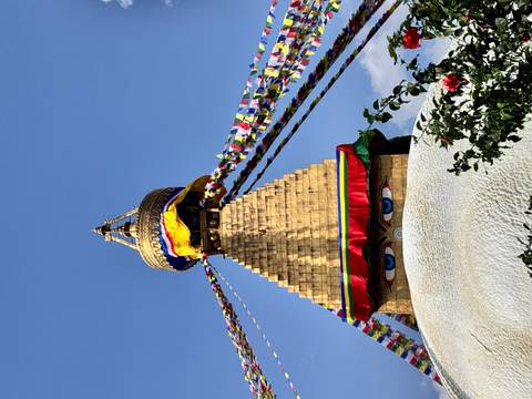 Baudhanath Stupa with prayer flags against blue sky.