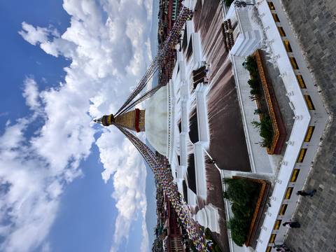 A wide view of Baudhanath Stupa under a cloudy sky.