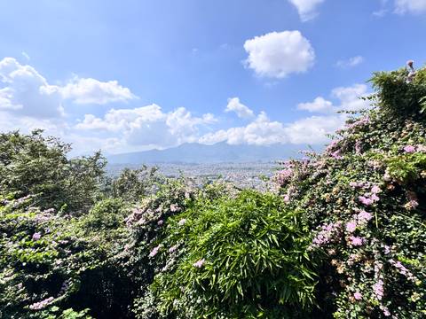 Wide view of a cityscape beneath a bright blue sky with fluffy clouds, possibly Kathmandu.