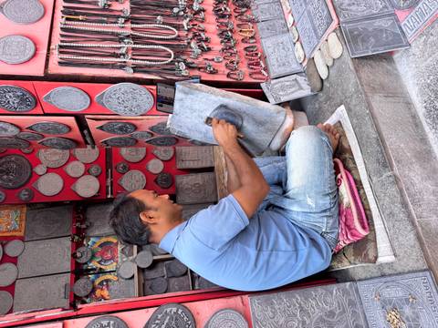       A man working on a stone carving in a shop filled with various plaques and decorations.
  