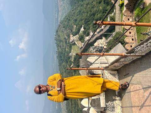       A person in traditional attire standing on a fort with a scenic view in the background.
  