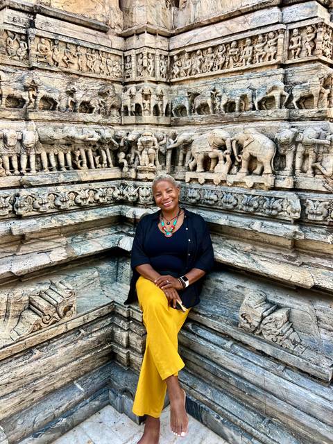       A person sitting in front of an intricately carved stone wall with elephant motifs.
  