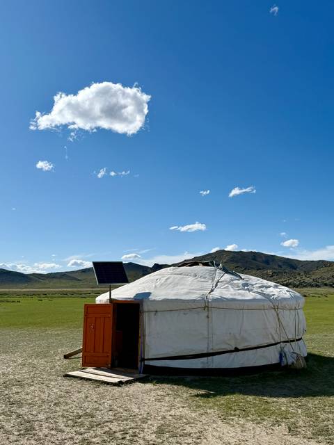 Traditional Mongolian yurt with solar panel in open landscape.